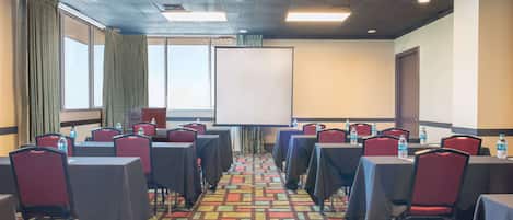A conference room with tables and chairs, a projector screen, and a carpeted floor.