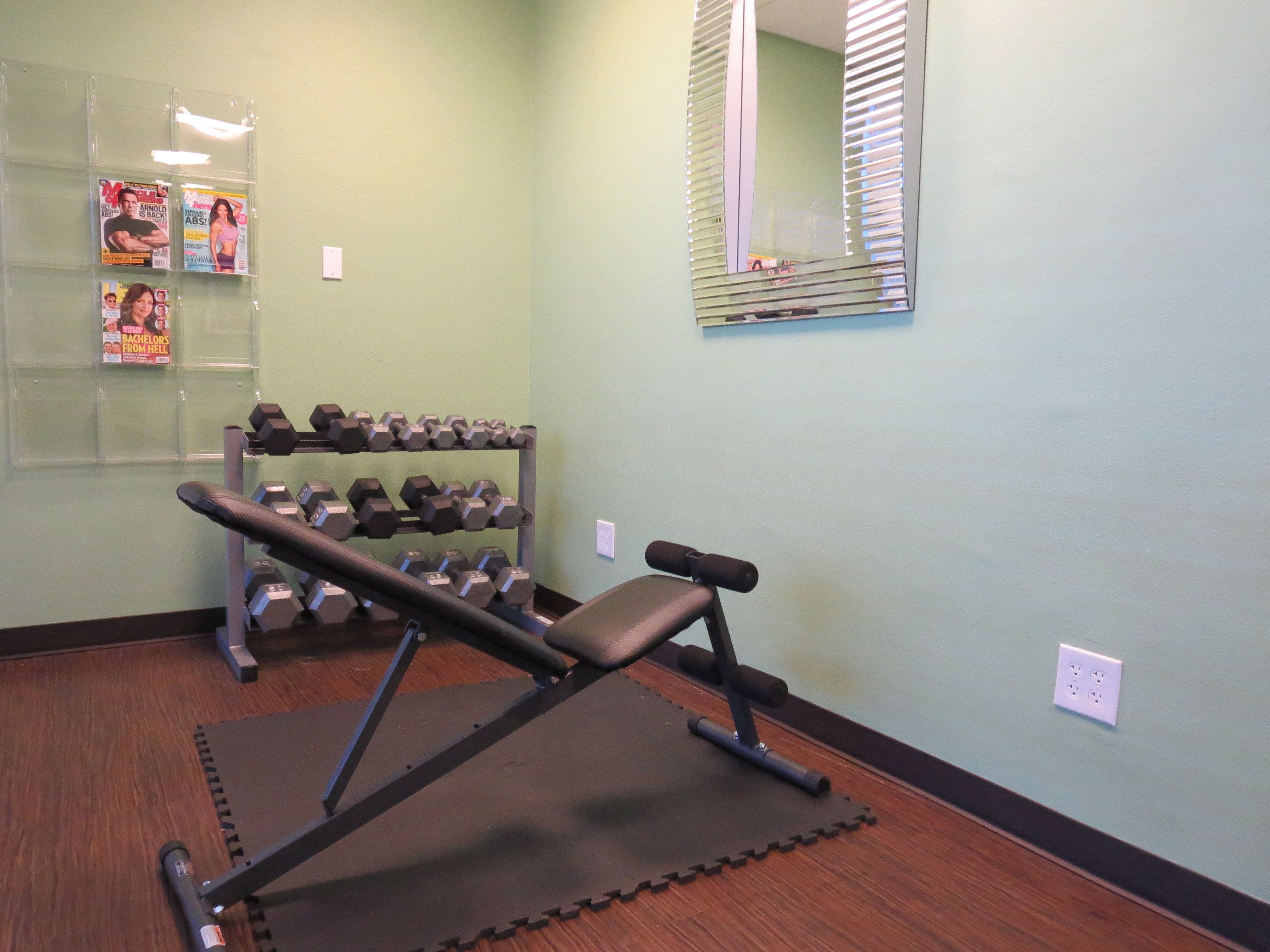A gym with a bench press, dumbbells, and a mirror on the wall.