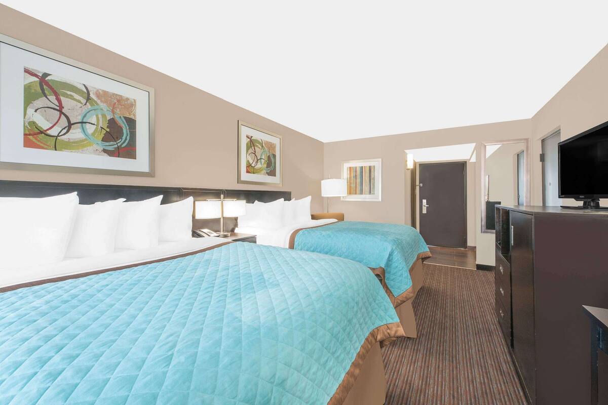 A hotel room with two beds, a TV, a desk, and artwork on the walls.