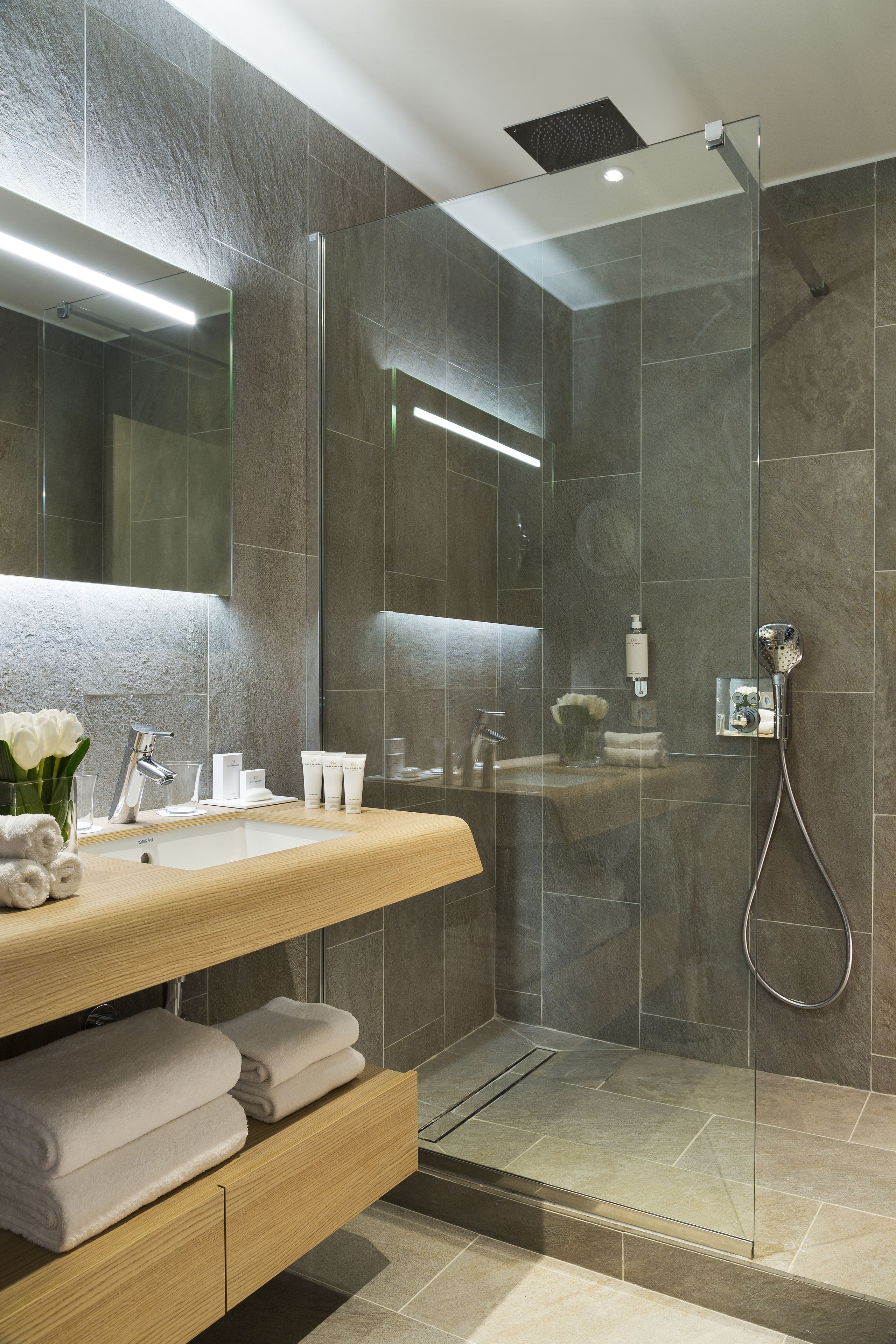 A modern bathroom with a glass-enclosed shower, a wooden vanity with a mirror, and a sink.