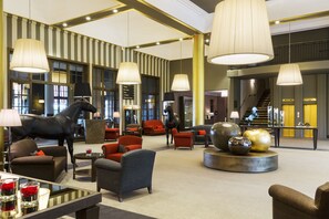 A spacious lobby with modern furnishings, a large horse statue, and a staircase leading to an upper level.