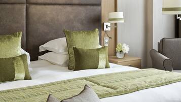 A neatly made bed with green and white pillows, a green and white checkered throw blanket, and a grey armchair.