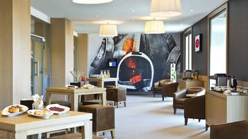 A modern hotel lobby with a dining area, seating, a large mural, and a reception desk.