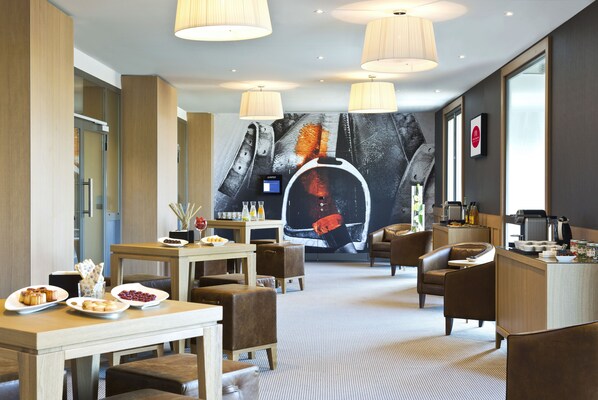 A modern hotel lobby with a dining area, seating, a large mural, and a reception desk. - Hôtel Barrière L'Hôtel du Golf Deauville (Saint-Arnoult)