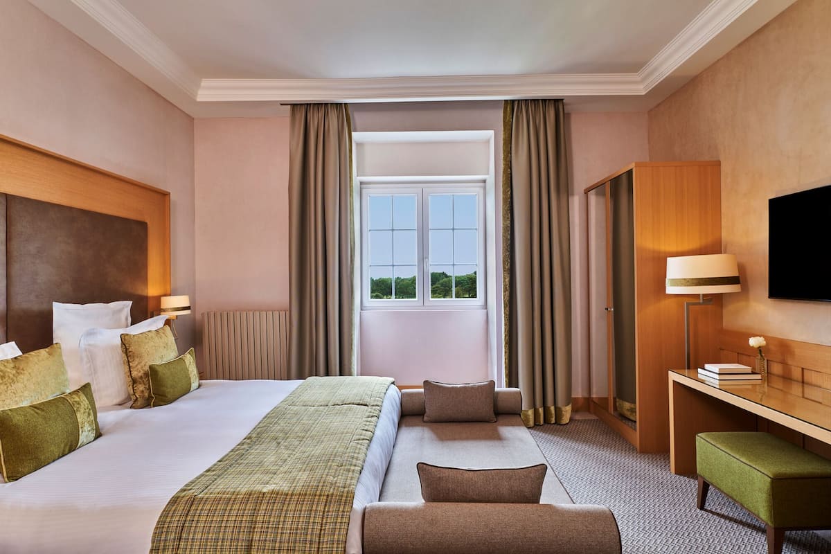 Ein Hotelzimmer mit einem großen Bett, einem Schreibtisch, einem Sessel und einem Fernseher.