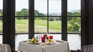 Mesa de comedor dispuesta con platos, vasos y cubiertos, con vistas a un campo de golf.