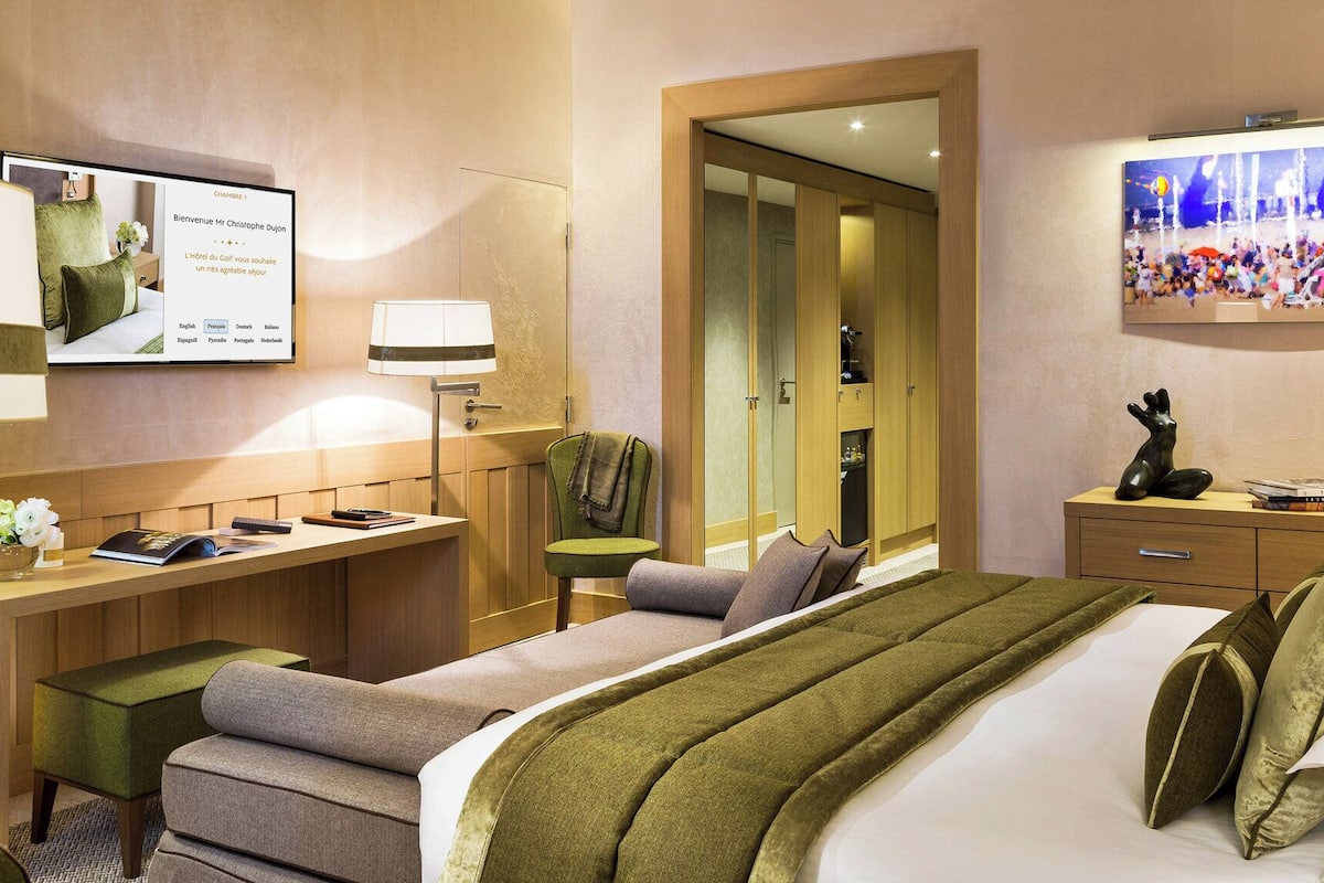 Ein Hotelzimmer mit Bett, Schreibtisch, Stuhl, Fernseher und einem Bild an der Wand.