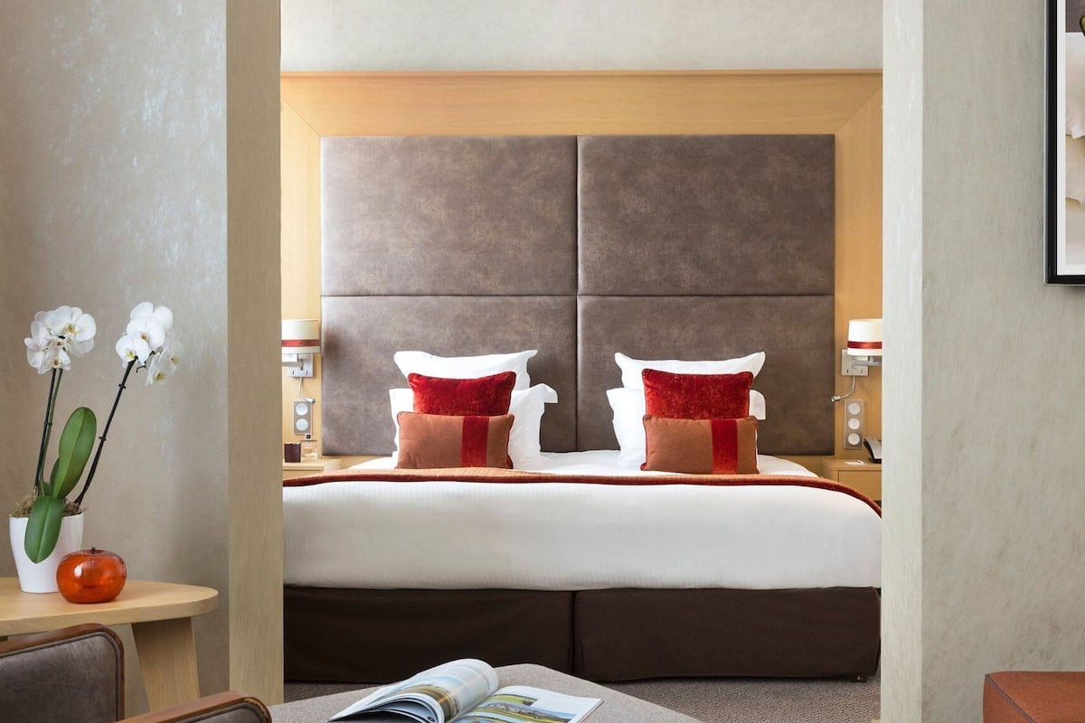 Ein Hotelzimmer mit einem großen Bett, zwei Nachttischen, einem Beistelltisch mit Lampe und einem gerahmten Bild an der Wand.