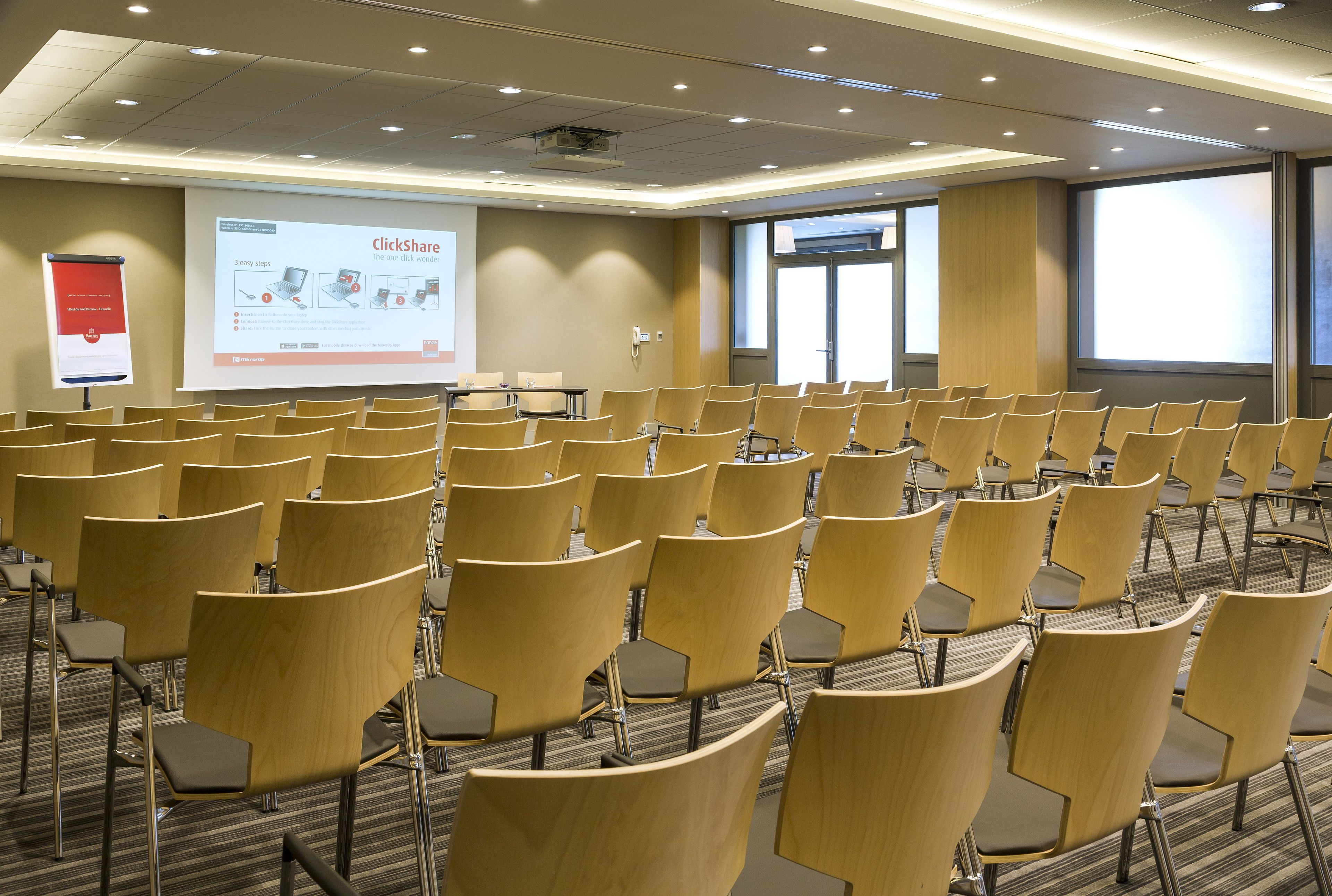 A conference room with rows of chairs, a projector screen, and a presentation on the wall.
