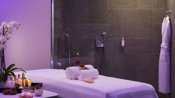 A spa room with a massage table, towels, a shower, and a plant.