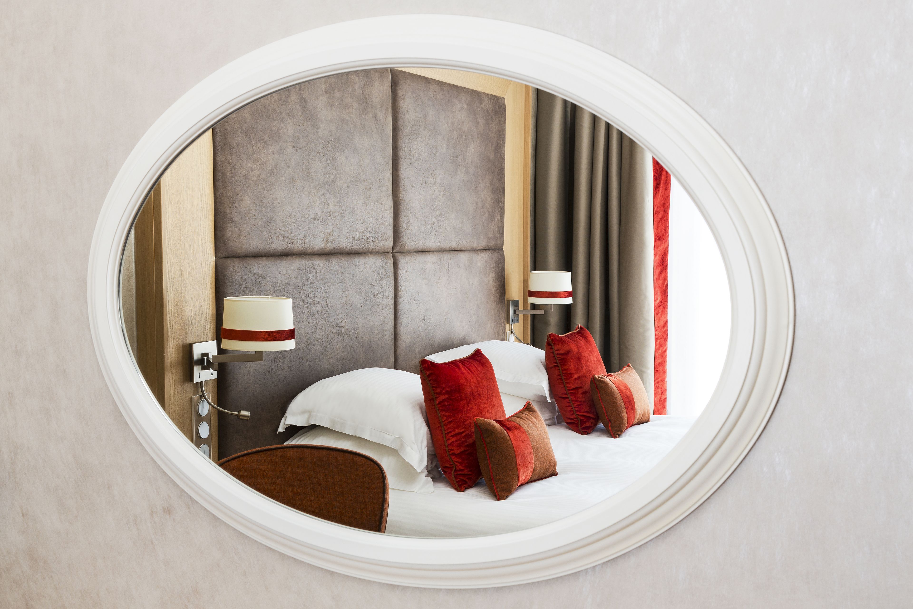 Una cama bien hecha con almohadas blancas y rojas, un cabecero y una lámpara de noche.