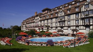 Un hotel con una amplia piscina rodeada de tumbonas y sombrillas, que presenta una arquitectura de estilo Tudor.