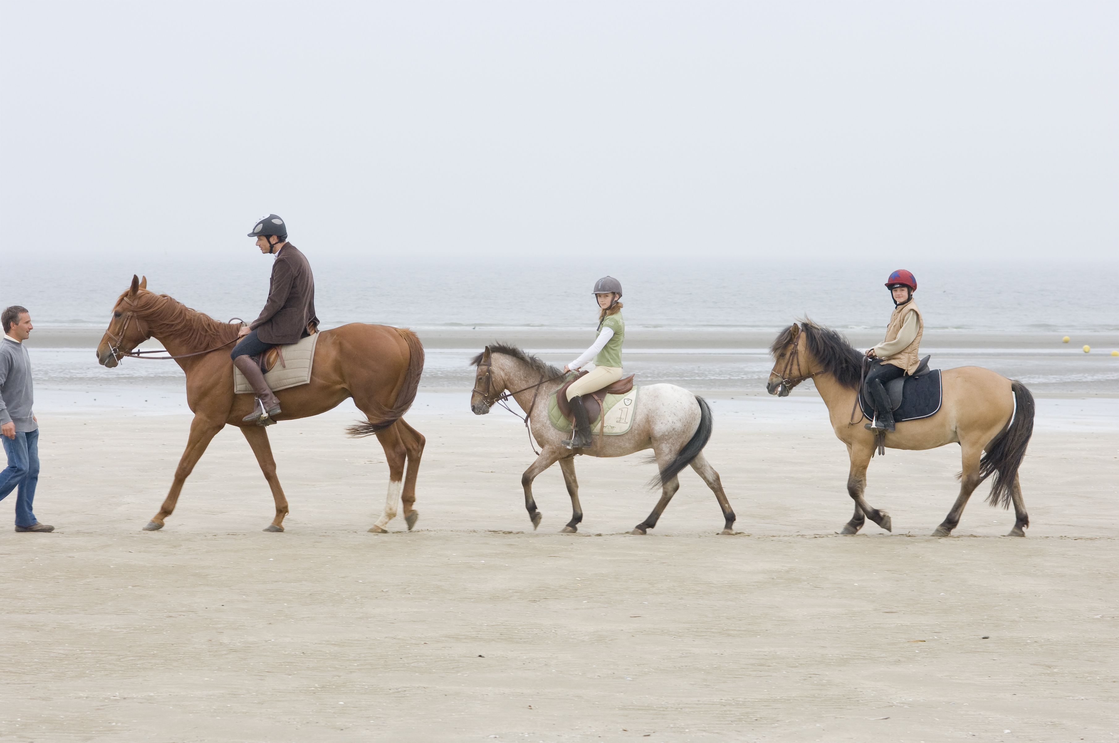 Escena de playa con tres caballos y jinetes.