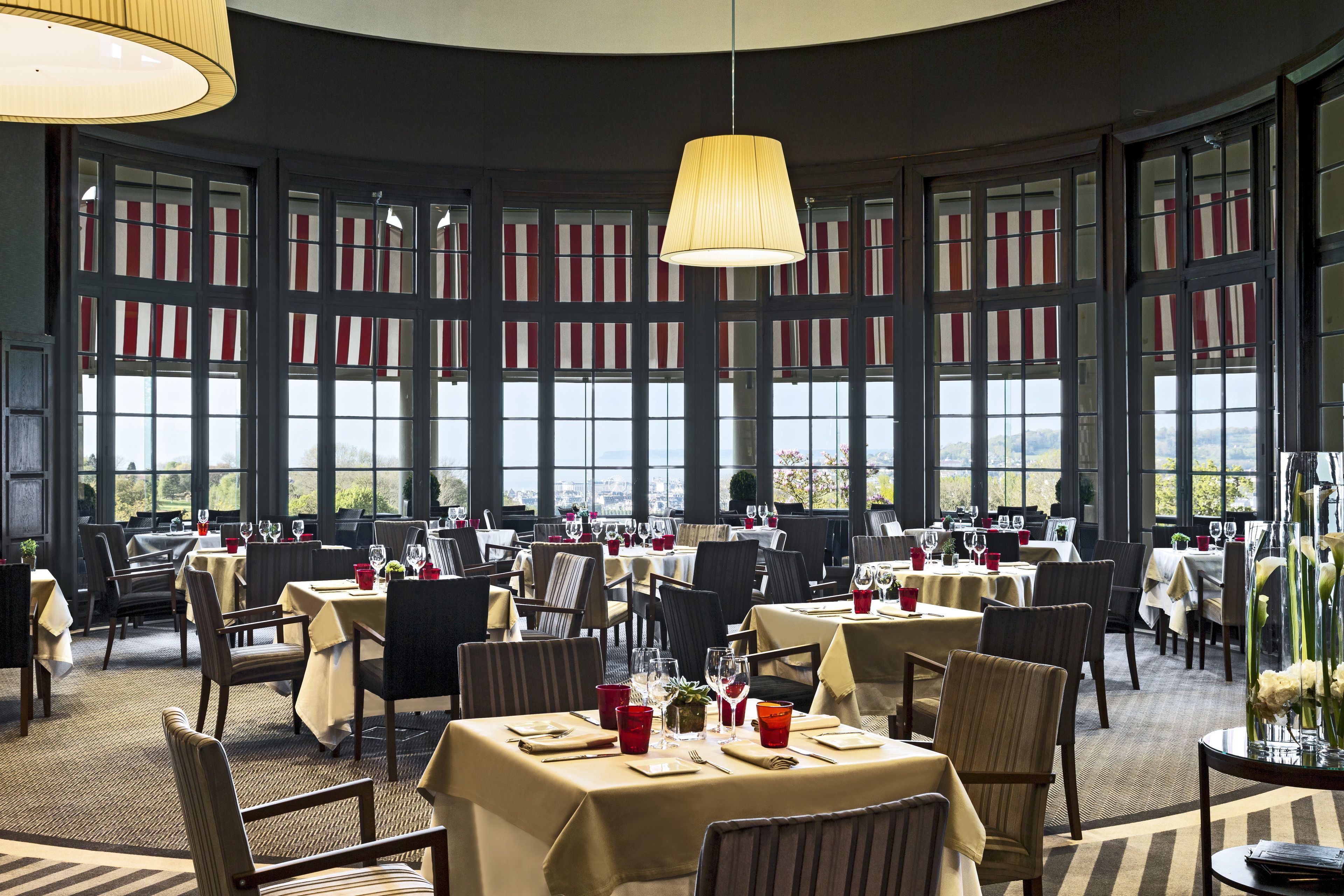 A restaurant with multiple tables and chairs, large windows, and a hanging light fixture.
