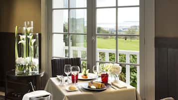 A dining table with a view of a golf course, a vase with flowers, and a bottle of champagne.