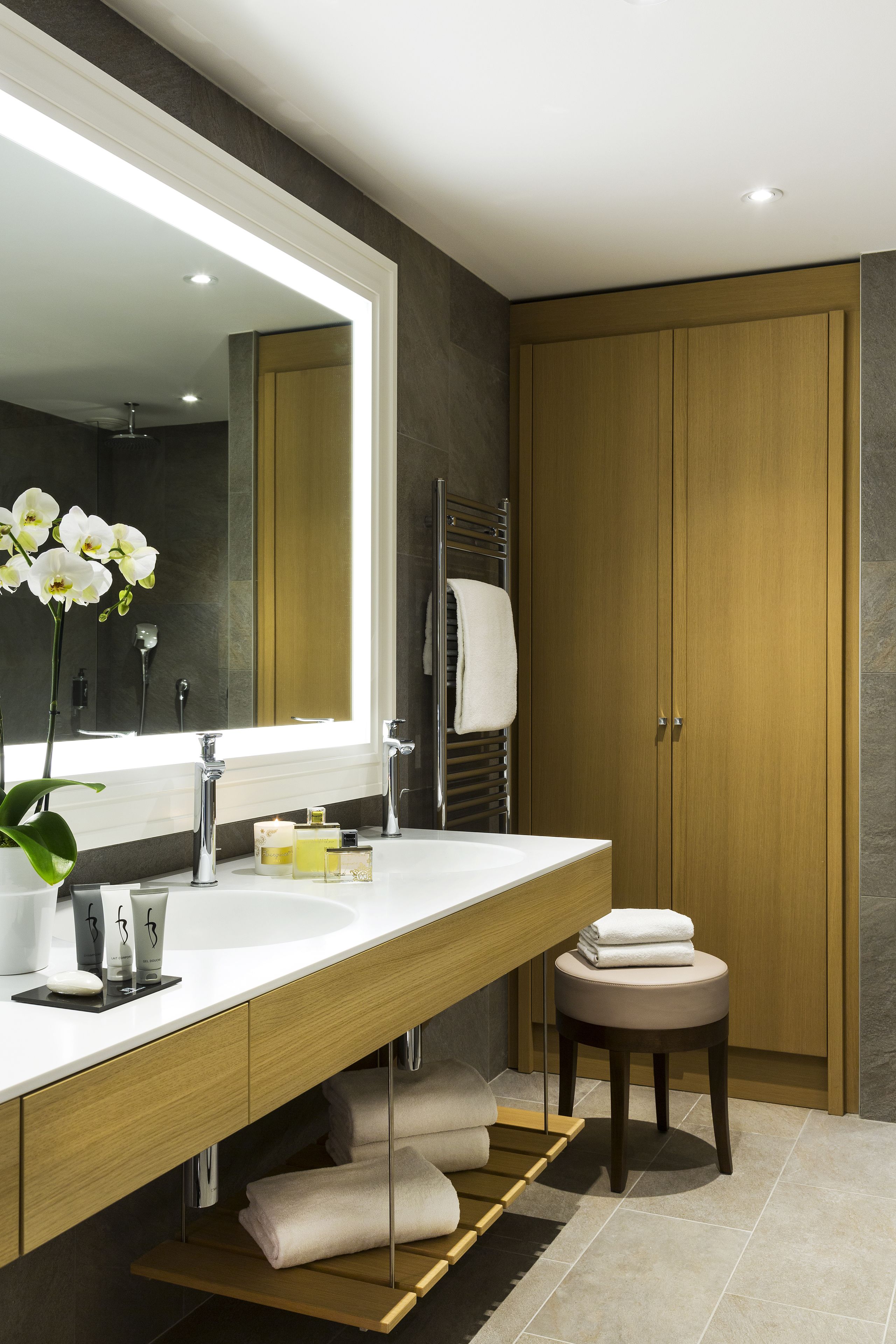Un baño moderno con un espejo grande, lavamanos dobles, un mueble de tocador de madera y un perchero para toallas.