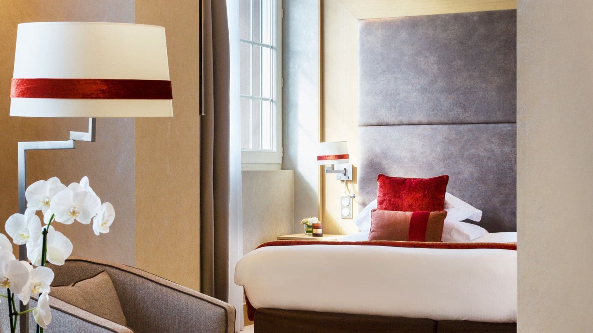A hotel room with a bed, a nightstand, a lamp, and a chair.