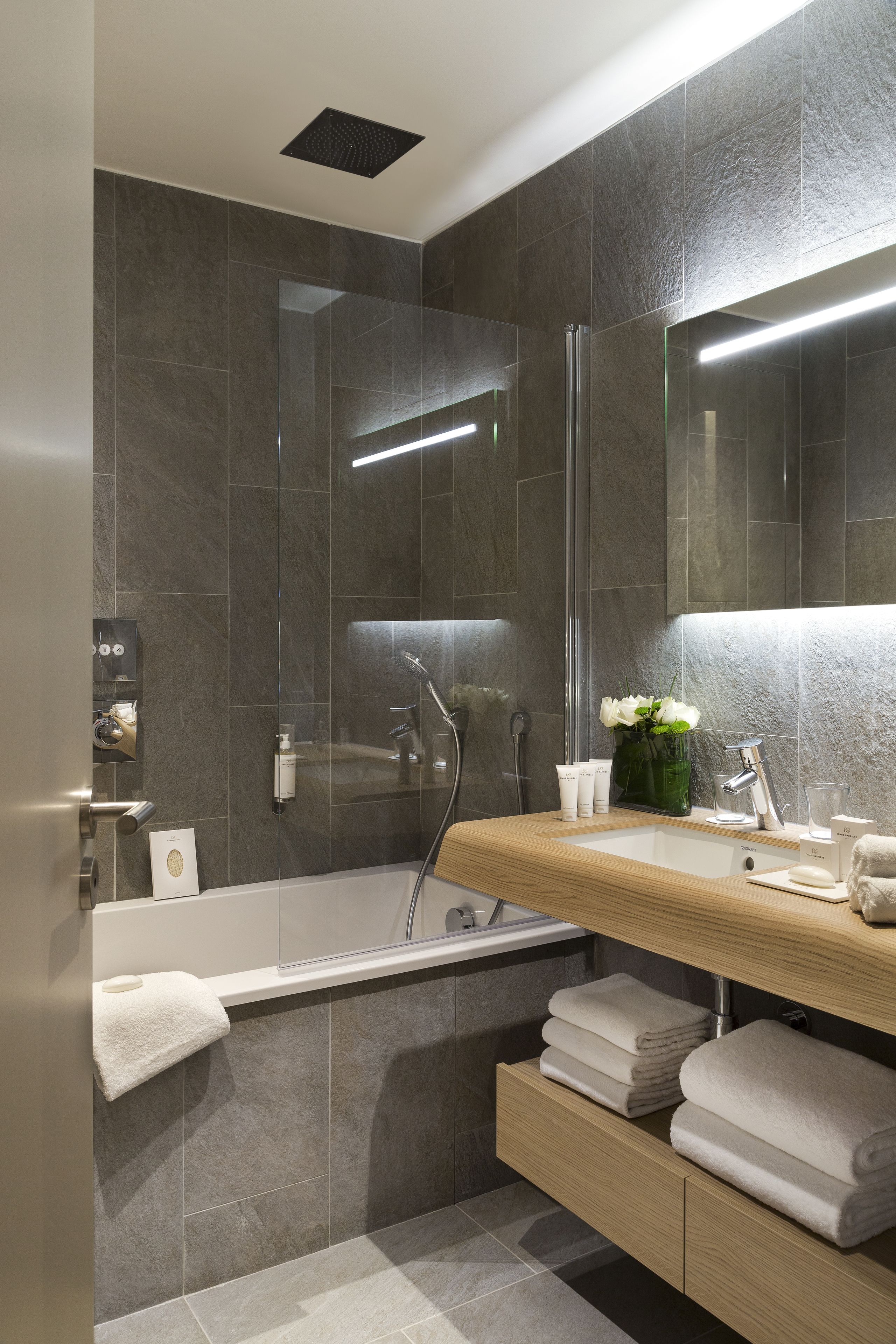 A modern bathroom with a bathtub, a glass shower enclosure, a vanity with a mirror, and a towel rack.