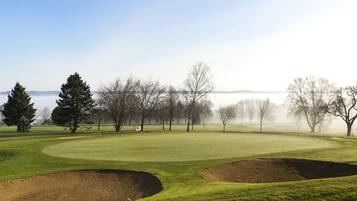A golf course with bunkers, trees, and a body of water in the background.