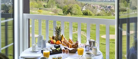 Een ontbijttafel met diverse gerechten en dranken, op een balkon met uitzicht op een golfbaan en stadsbeeld.