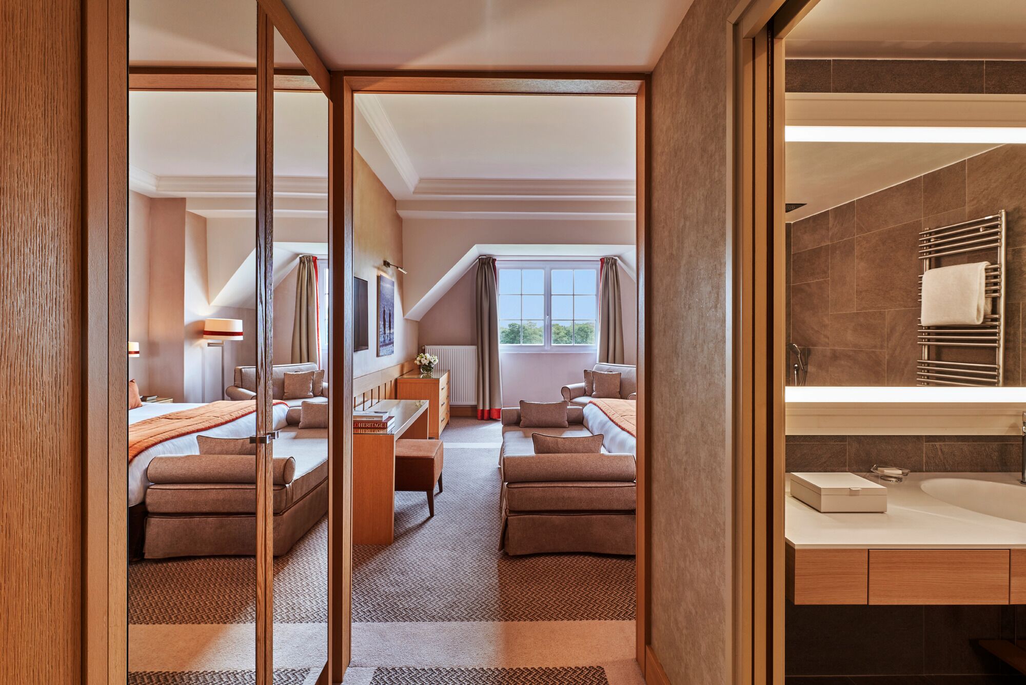 Une chambre d’hôtel moderne dotée d’un grand lit, d’un coin salon avec une table, et d’une salle de bain séparée avec une baignoire et un grand miroir.