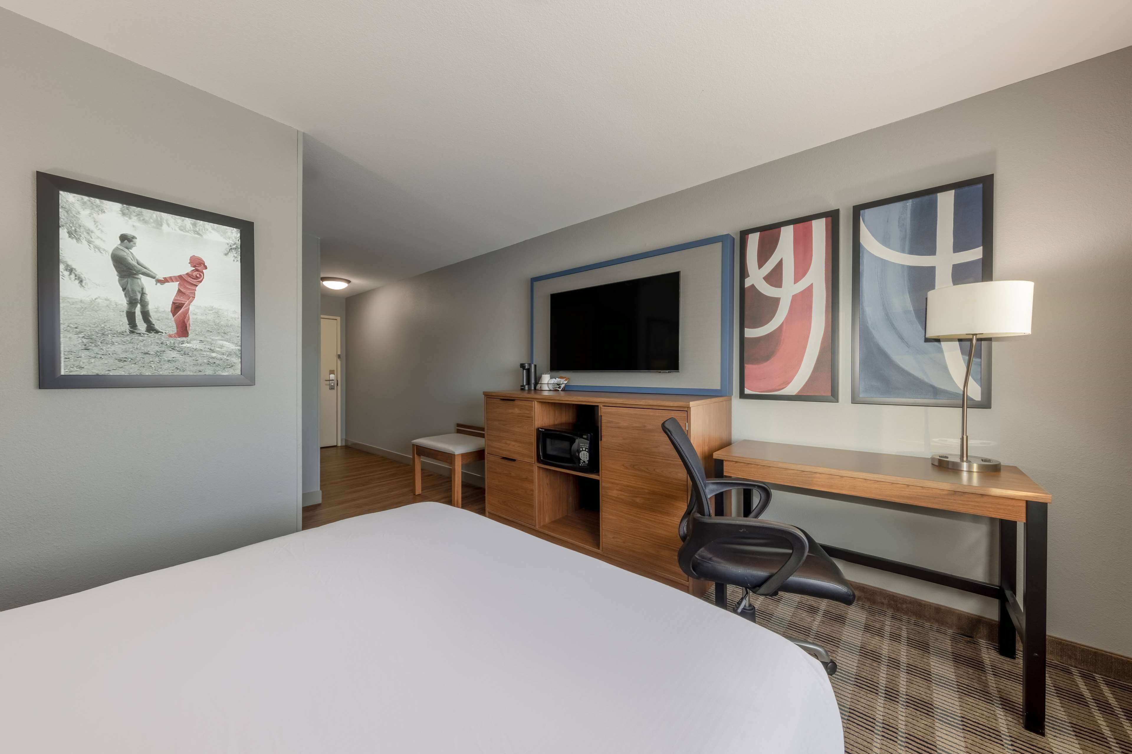 A hotel room with a bed, a desk, a chair, a TV, and artwork on the walls.