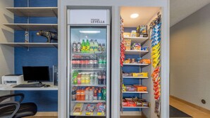 A vending machine with a variety of drinks and snacks, a computer setup, and shelves with packaged goods.