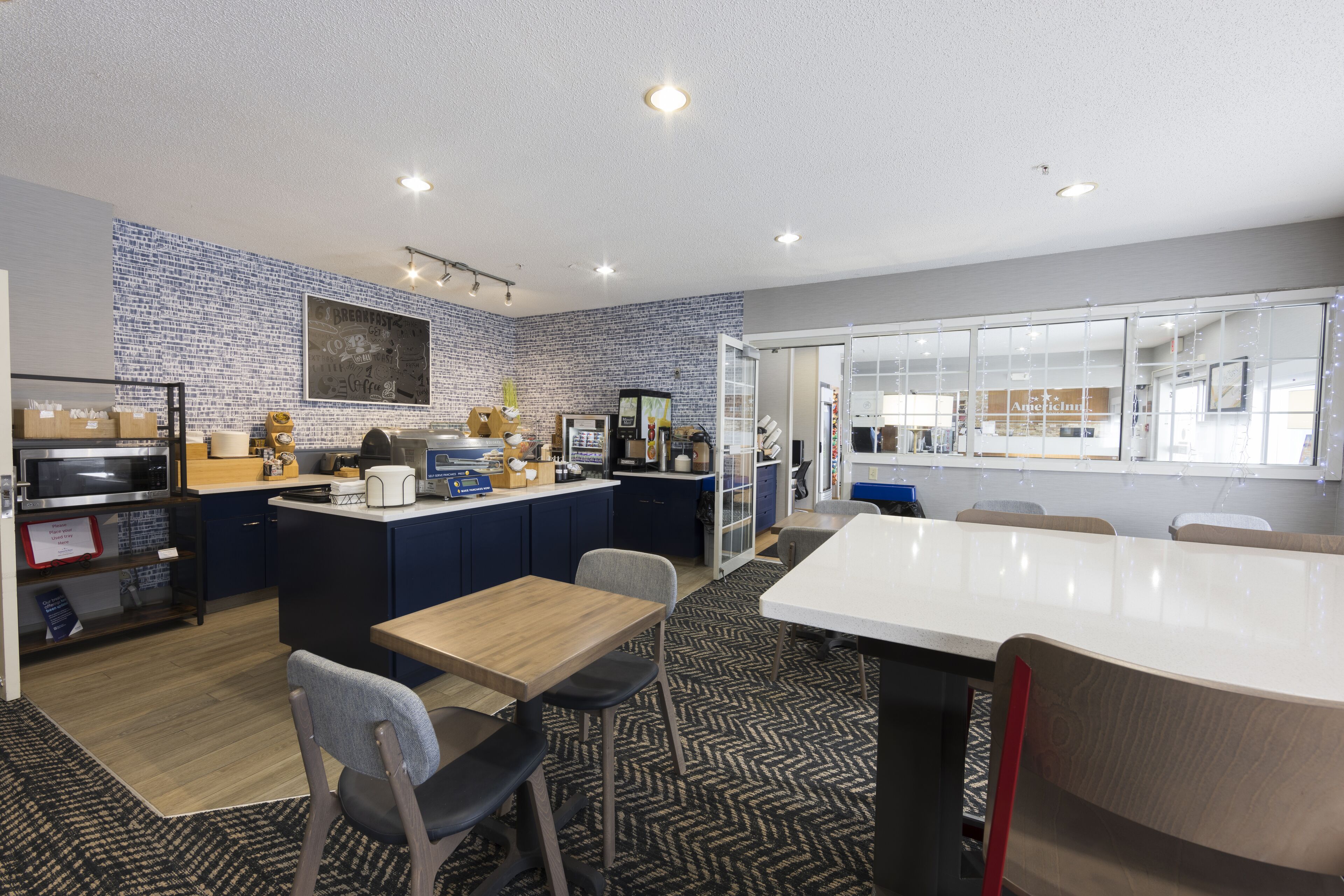 A modern kitchen with a central island, a dining area with a long table, and a view of a store through glass doors.