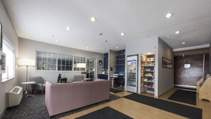 A hotel lobby with a reception desk, seating area, and a refrigerator stocked with beverages.