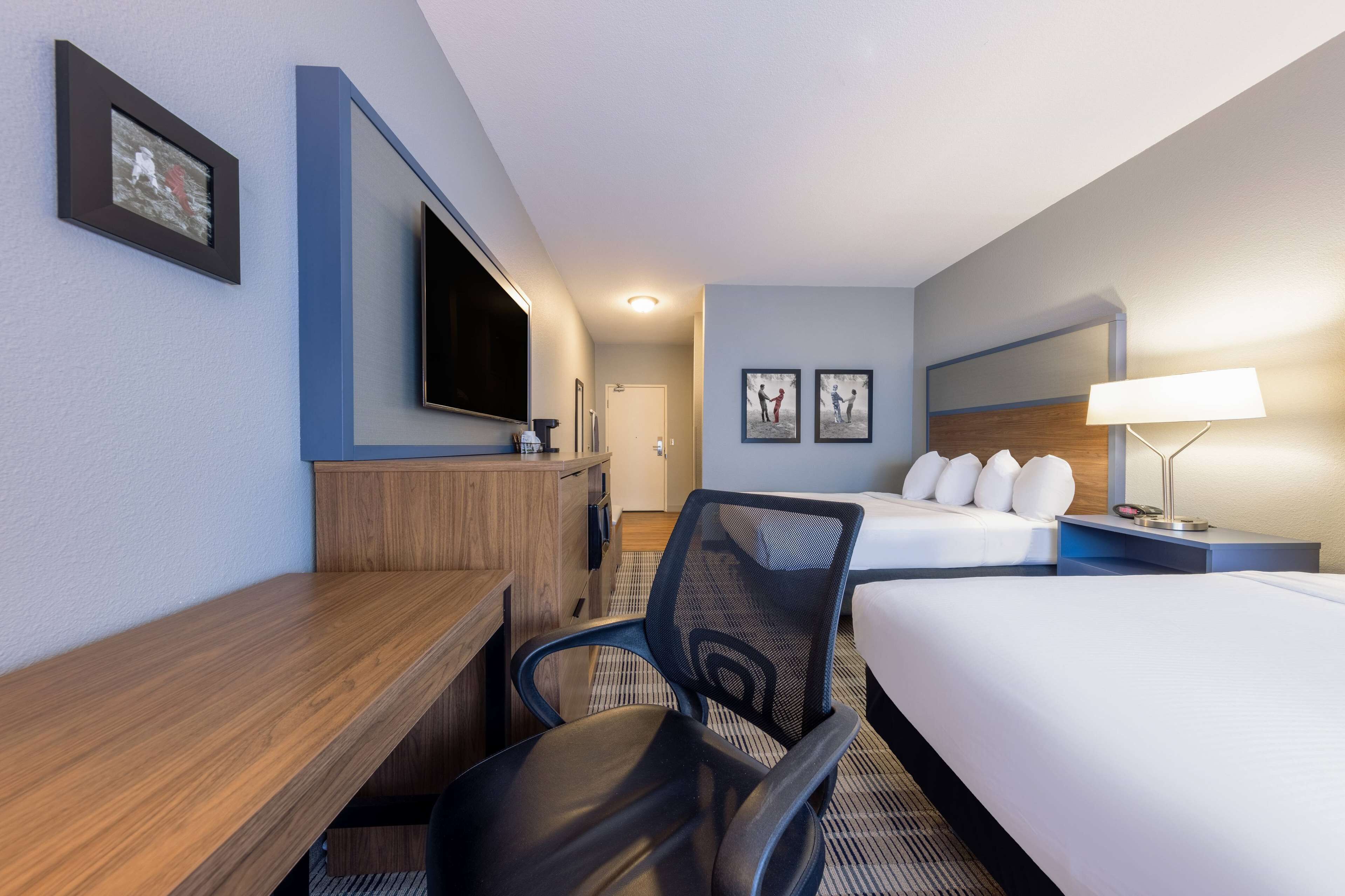 Une chambre d’hôtel comprenant un lit, un bureau avec une chaise, une télévision et deux tableaux encadrés accrochés au mur.