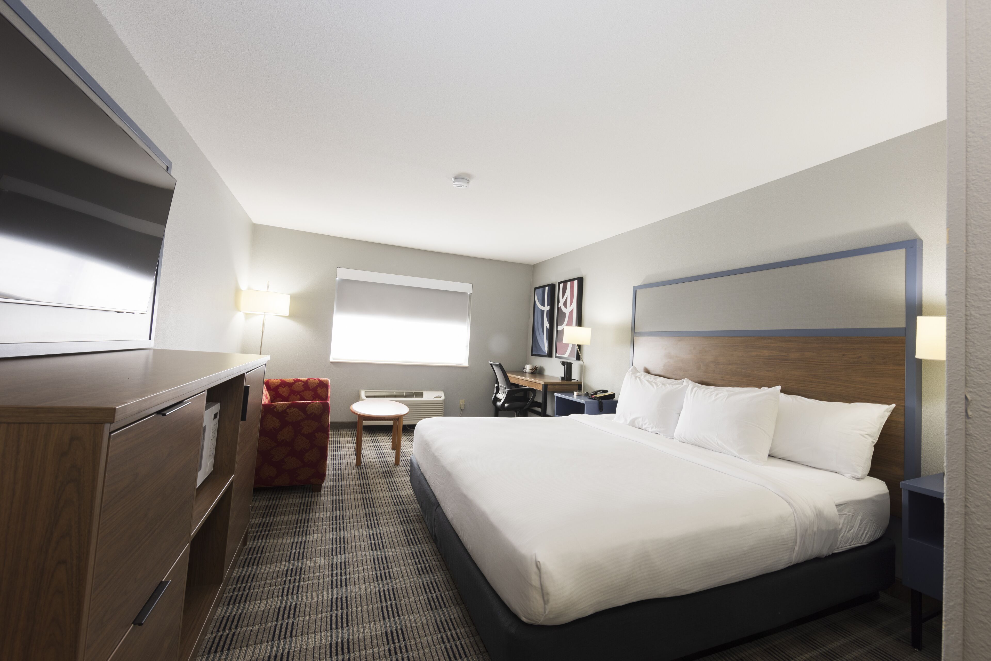 A hotel room with a large bed, a desk, a chair, a small table, and a TV.