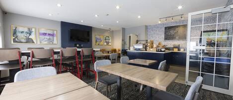 A modern dining area with wooden tables and chairs, a kitchen area with a chalkboard menu, and artwork on the walls.