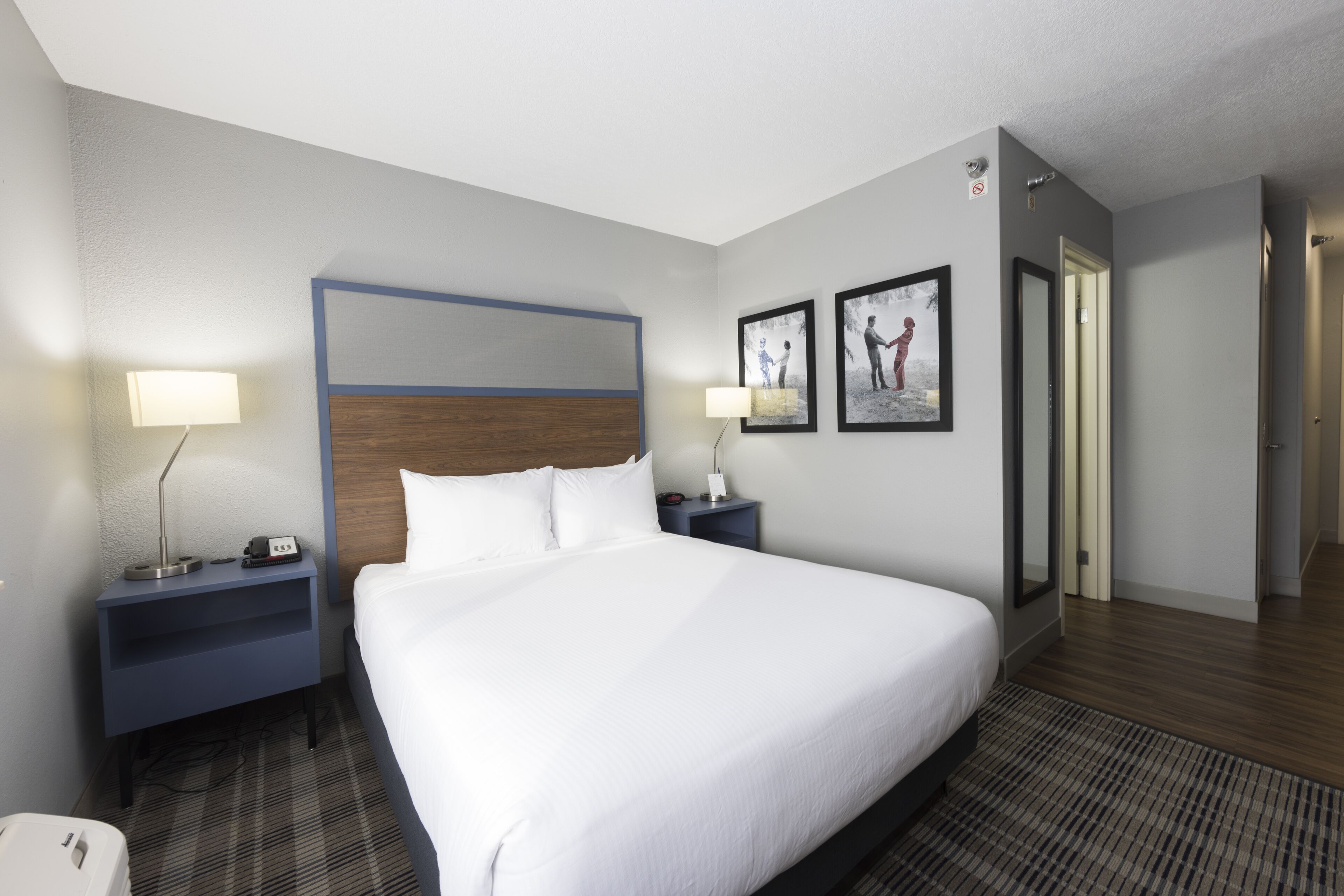 A hotel room with a large bed, two bedside tables, a nightstand, a lamp, and two framed pictures on the wall.