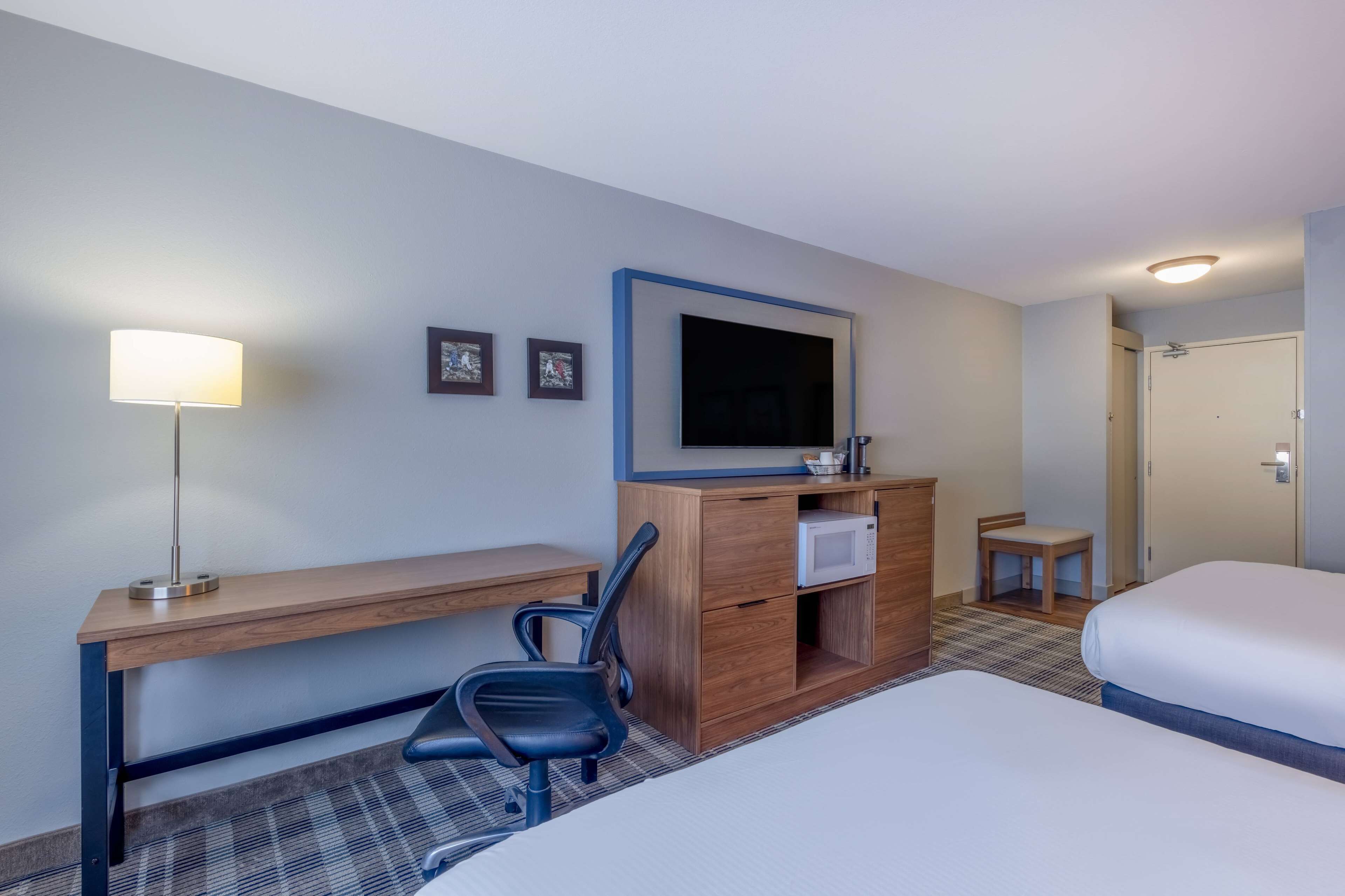 A hotel room with a bed, a desk with a chair, a television, a microwave, and a small table with a chair.