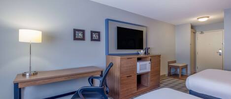 A hotel room with a bed, a desk with a chair, a television, a microwave, and a small table with a chair.