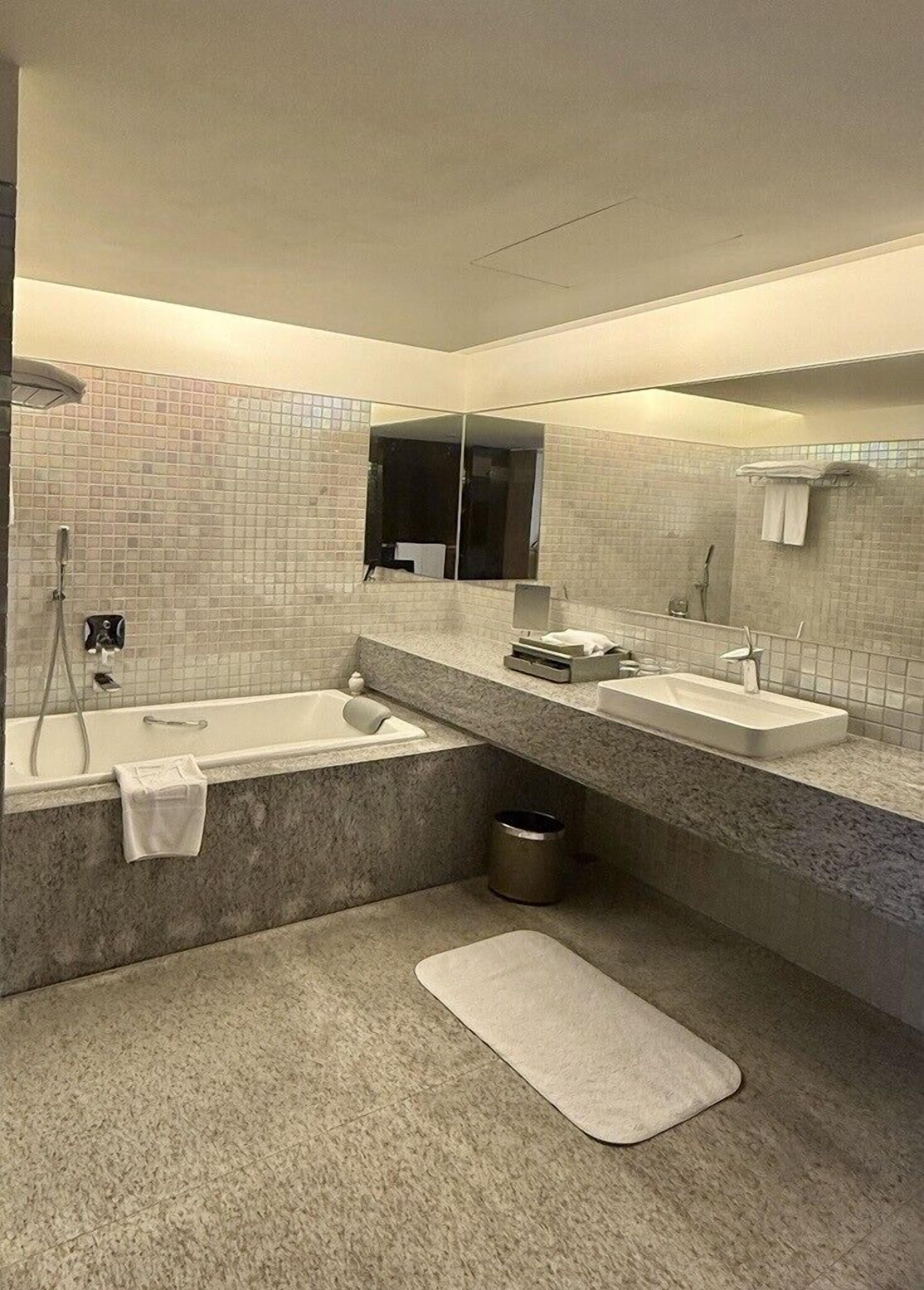 A modern bathroom with a bathtub, two sinks, a large mirror, and a shower.