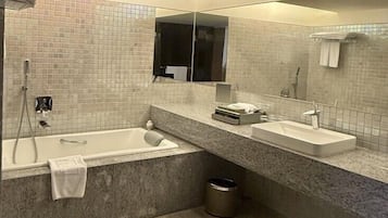 A modern bathroom with a bathtub, two sinks, a large mirror, and a shower.