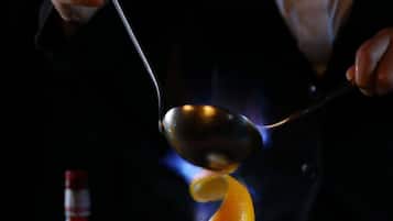 A person performing a culinary technique with a spoon over a flame.
