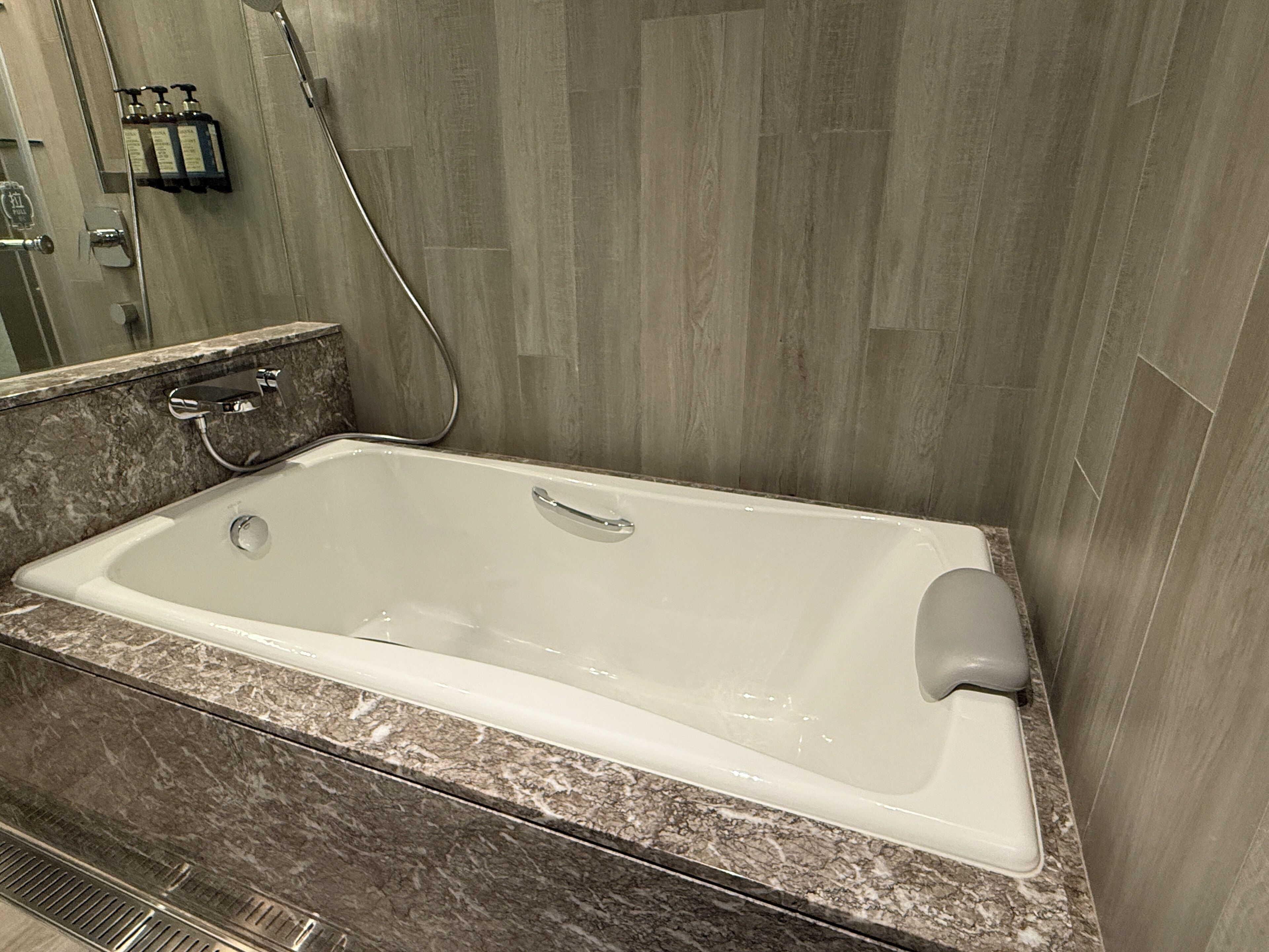Un baño moderno con una bañera rectangular, un cabezal de ducha de mano y un mostrador de mármol.