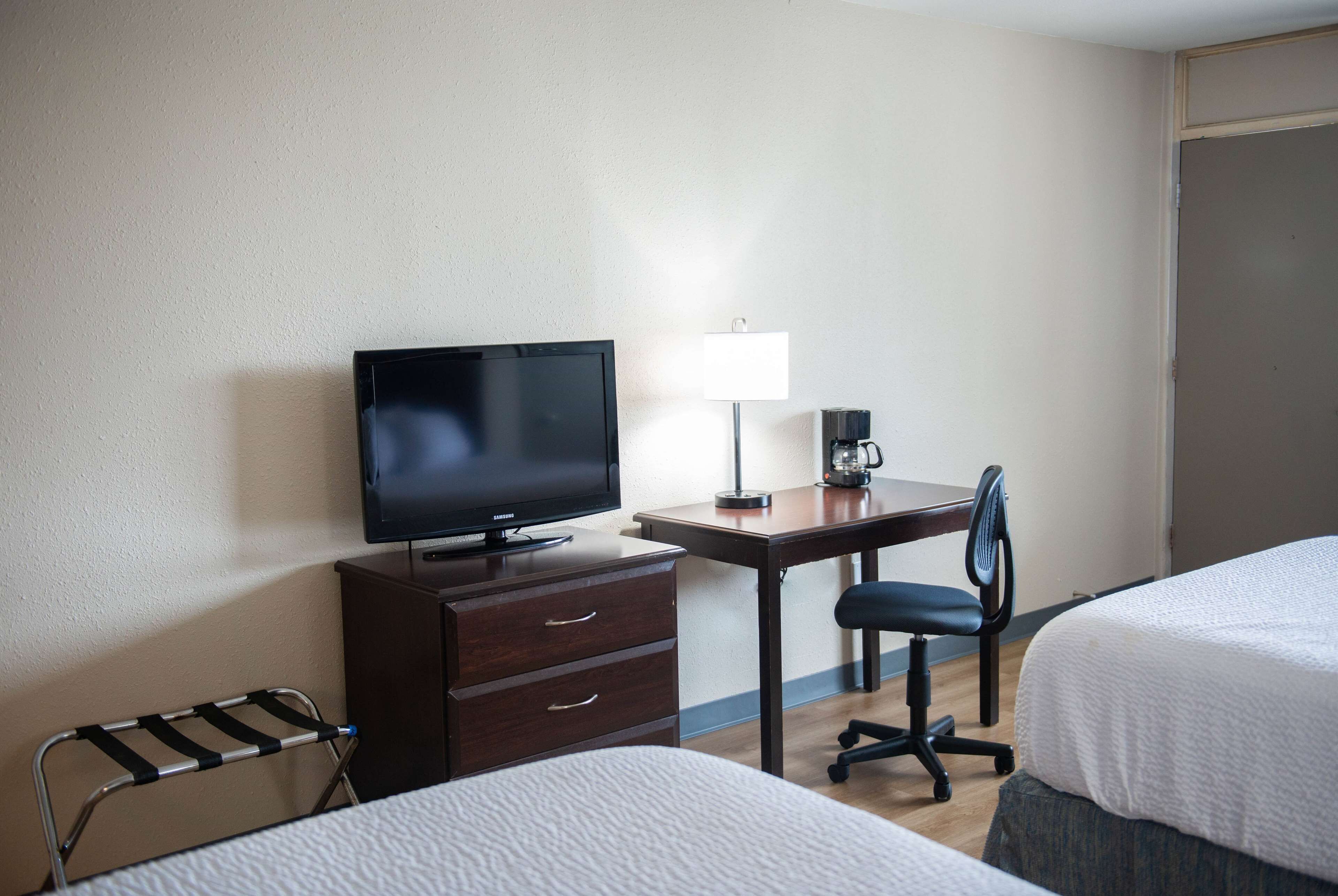 A hotel room with a bed, a desk with a computer, a chair, a TV, and a lamp.