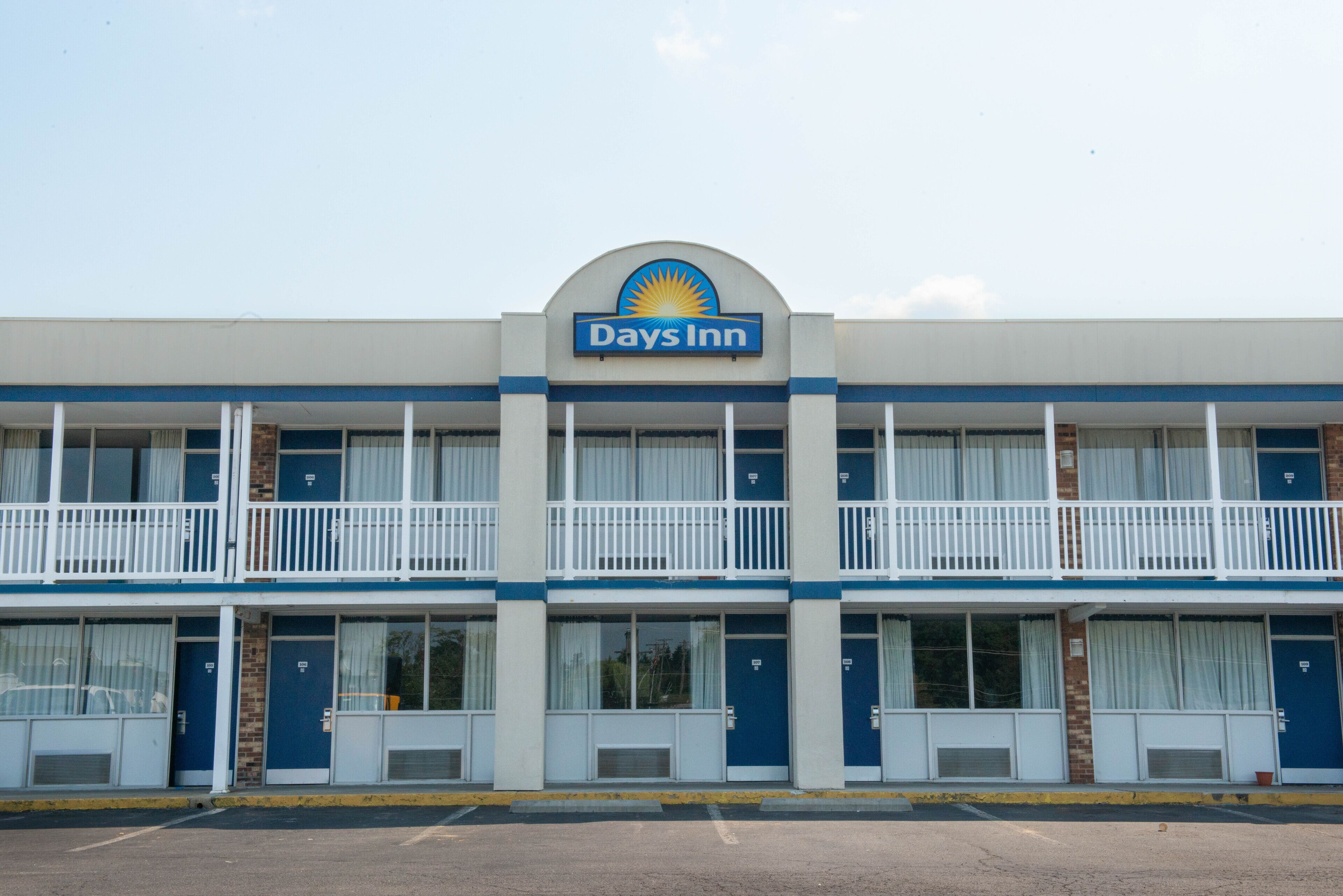 Un bâtiment de la chaîne Days Inn aux couleurs bleu et blanc, avec une enseigne portant le logo Days Inn, plusieurs balcons et un parking situé à l’avant.