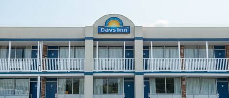 Un edificio de Days Inn con una combinación de colores azul y blanco, que presenta un letrero con el logotipo de Days Inn, varios balcones y un estacionamiento al frente.