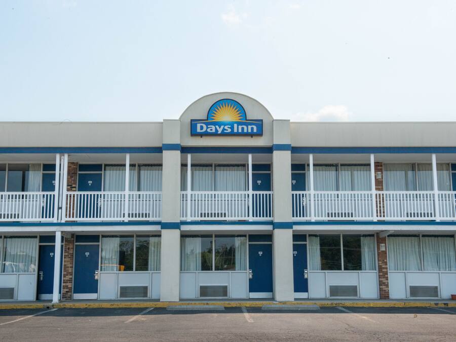 Een Days Inn gebouw met een blauw-wit kleurenschema, voorzien van een bord met het Days Inn logo, meerdere balkons en een parkeerplaats ervoor.