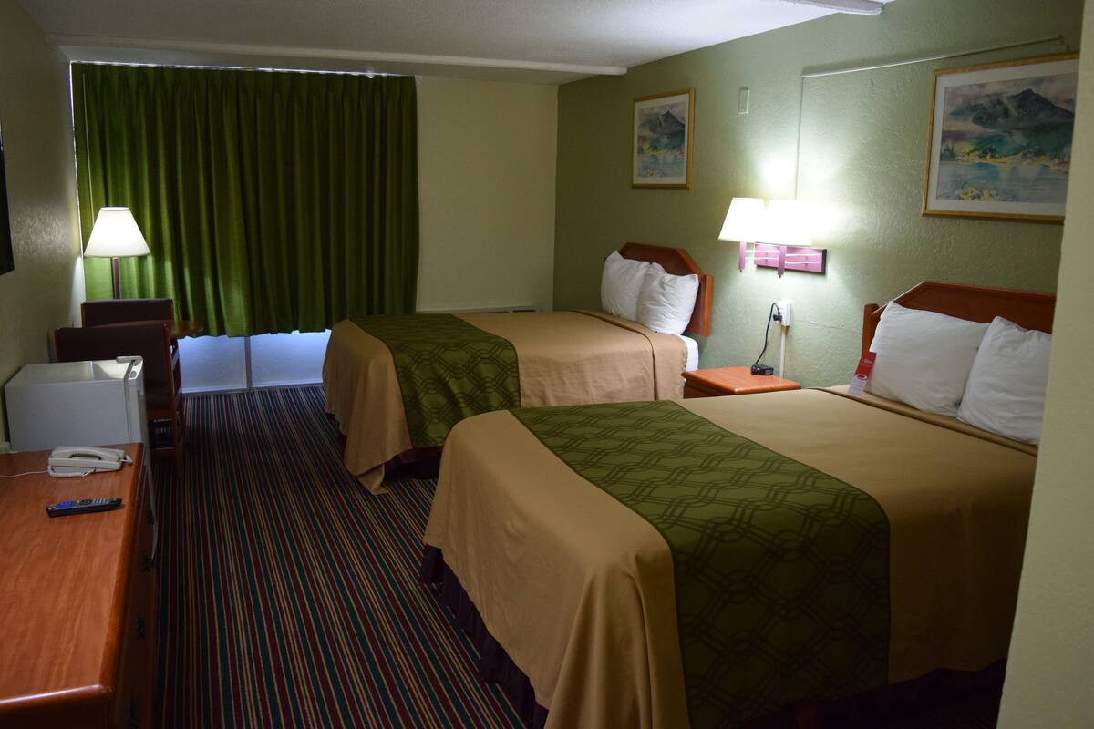 A hotel room with two beds, a desk, a telephone, and a lamp.