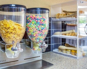 Two beverage dispensers with a kitchen counter and a storage rack with baked goods.