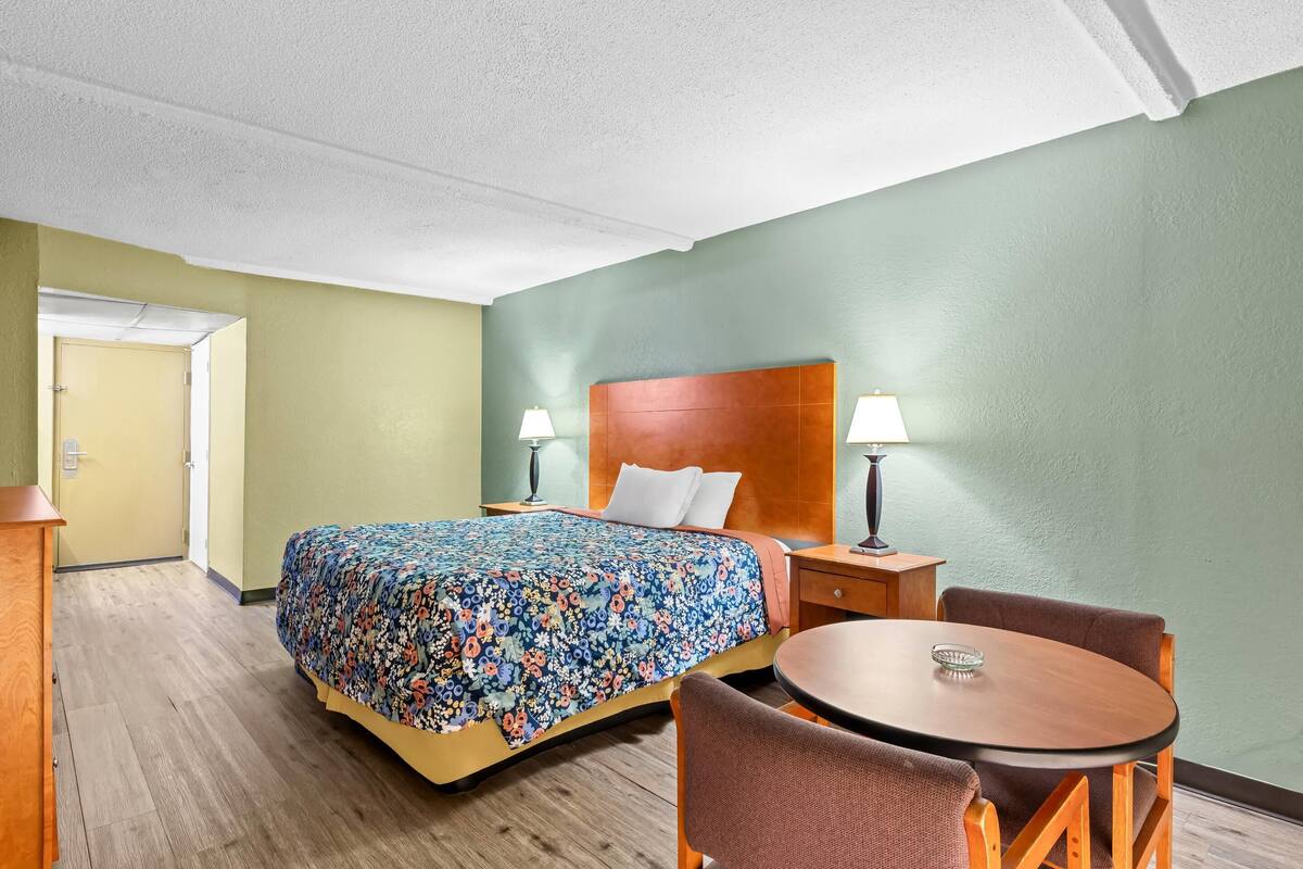 A hotel room with a bed, bedside tables, a round table, and chairs.