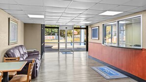A lobby with a leather sofa, a table, and chairs, a wooden floor, and a view through glass doors to the outside.