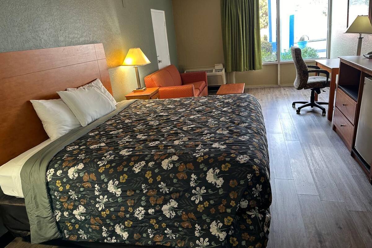 A hotel room with a bed, a desk, a chair, and a window with curtains.