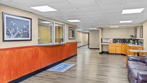 A hotel lobby with a reception desk, framed cityscape pictures, a wooden floor, a kitchenette, and a leather sofa.