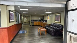 A hotel lobby with a reception desk, a seating area with a couch and table, a kitchenette, and framed artwork on the walls.